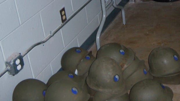 Stacks of M1 steel helmets with 29th Division insignia on the armory floor before sequence numbers were assigned.