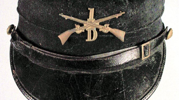 Model 1895 kepi originally worn Infantry Private Bert M. Bartlett, a railroad worker from Devils Lake, North Dakota. The solid brass branch insignia with a screw-post fastener on the reverse replaced the Pattern 1872 branch insignia in 1896.