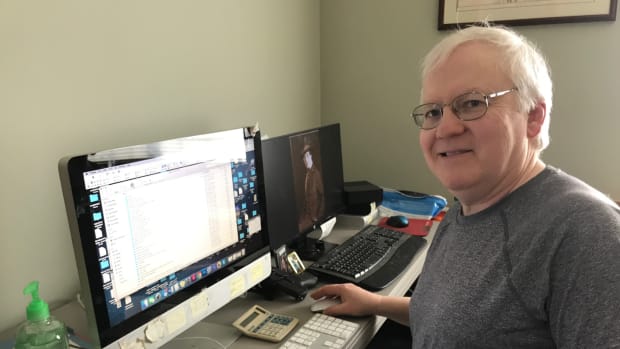 Photo of John Adams-Graf in temporary office space with hand sanitizer, two computers, and a pistol on his desk.