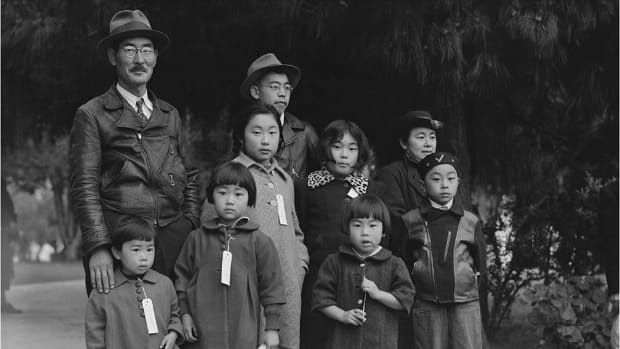 The Mochida family, wearing identification tags awaits a bus. They were forced to leave their two-acre nursery and greenhouse in Eden, California, May 1942.