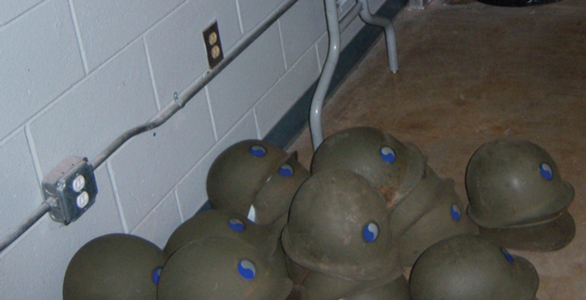 Stacks of M1 steel helmets with 29th Division insignia on the armory floor before sequence numbers were assigned.