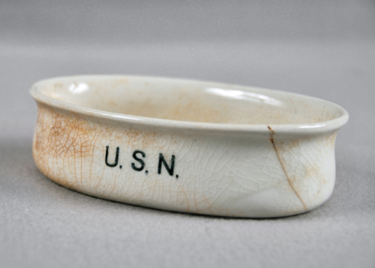  A white ceramic soap dish from the USS San Diego. The interior has a ridged bottom. “USN” is written on the side of the dish in black. There are no maker’s marks.