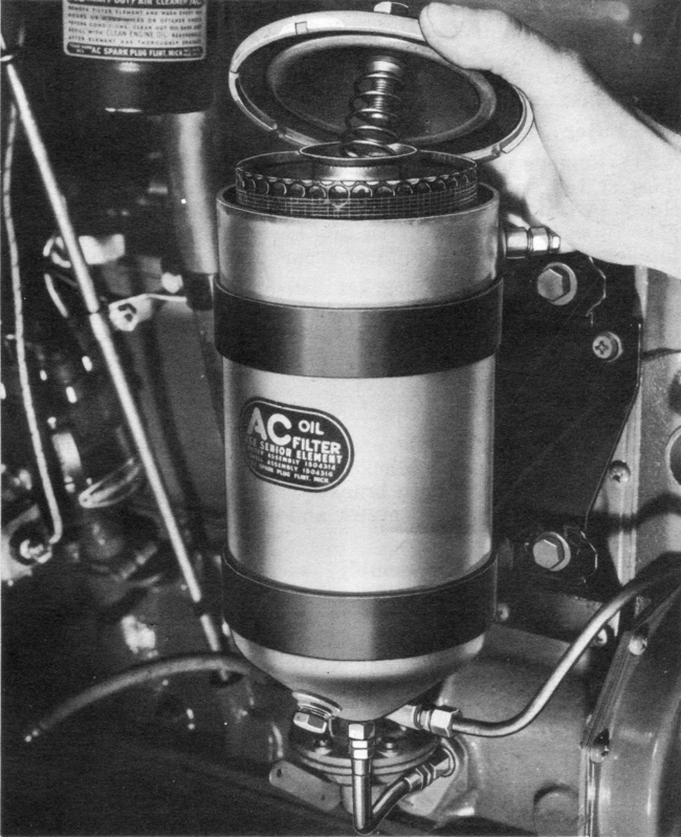  Removing the top cover from a typical Military Standard Senior bypass type oil filter. Note the spring on the cover securing bolt. After removing the cover, remove the drain plug in the bottom of the filter case and drain the oil into a suitable container. Be patient, as it will take some time for most of the oil to drain out of the element