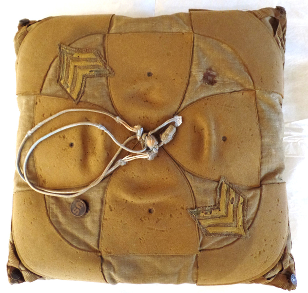  The top of the pillow found in the Rector House in 2018 is decorated with a cross pattern in the center. It, and the corners, were made from a campaign hat. The other surface areas were made from uniform material. Also visible are a collar disk, campaign hat cord, a pair of sergeant’s stripes (a souvenir perhaps), and service coat pocket buttons on the corners.