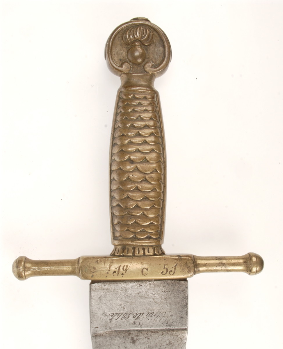 he cast brass hilt of the Artillery and Engineers machete featured a fish scale grip and a flaming bomb emblem on the pommel. The cross guard will often be unit marked, as seen here. This particular example was manufactured at Toledo in 1844.