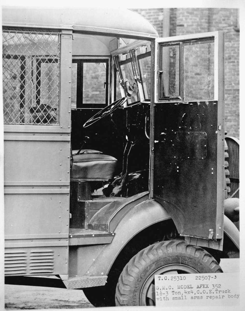  The cab is viewed through the open right door. The door has a vent window in addition to a roll-down window. On the center column of the windshield is a four-bladed fan, part of a windshield defroster.