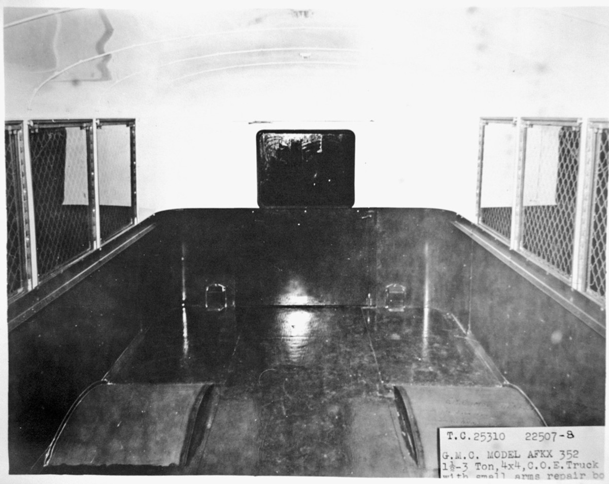 The interior of the small-arms-repair body of an AFKX-352 is viewed from the front, with the window of the rear door at the center. The interior paint is glossy. Just above the floor to each side of the door is a box enclosing a taillight and its electrical wire. No ordnance shop equipment has been installed inside yet.
