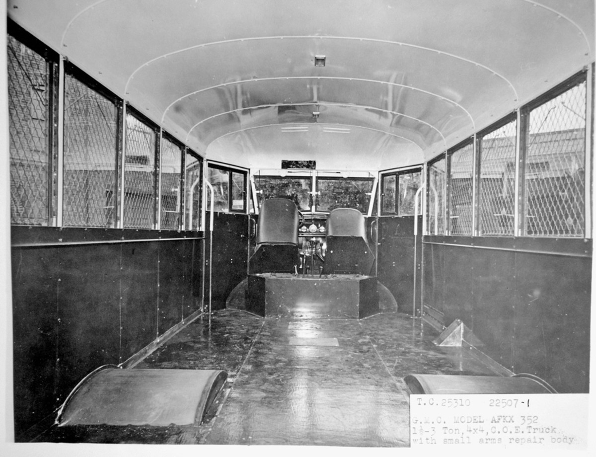  The interior of the body and the cab of an AFKX-352 with small-arms-repair body are seen from the rear of the body. The two seats in the cab were mounted on pentagonal plates that were hinged at the front, and they are tilted forward in this view. The wedge-shaped object between the left rear wheel well and the right cab door is an enclosure for the fuel filler neck.