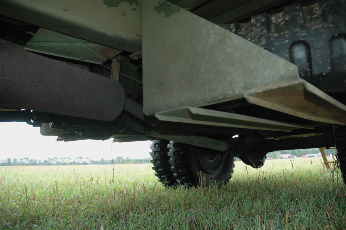 As seen from under the left side of the chassis, to the left is the muffler, and to the right is the spare tire and its carrier. The carrier features triangular end pieces with two steel channels welded to their bottoms. The rear axle in the background is the Timken Model 53624-NX2, with a split-type housing and a differential gear ratio of 6.6:1.