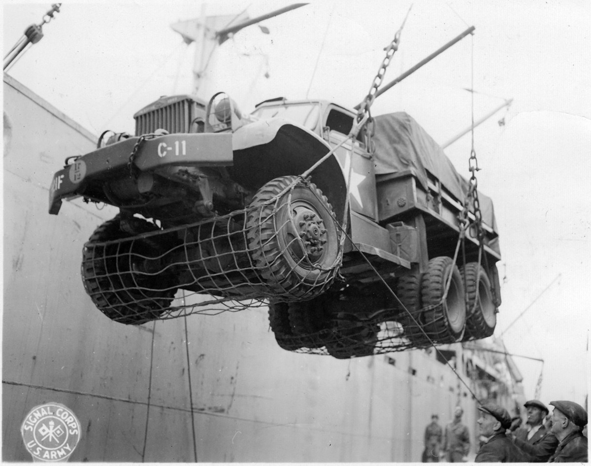 At an unidentified port, a Model 968 truck destined for Normandy is being hoisted by cargo nets aboard a transport ship on July 13, 1944. A five-gallon liquid container is strapped to the front of the forward left mudguard. The vehicle was assigned to Battery C, 21st Field Artillery Regiment, U.S. 5th Infantry Division.