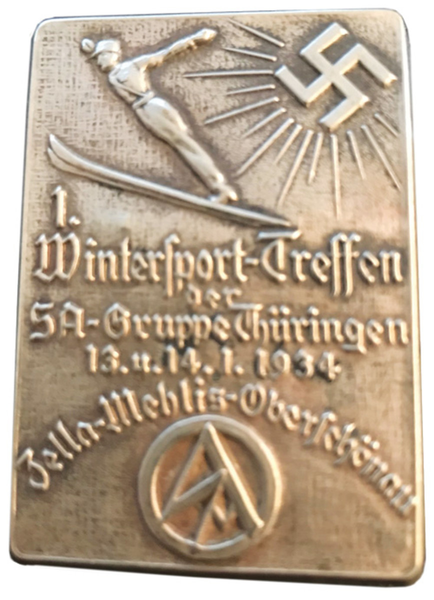A 1934 SA Gruppe Thuringen 1st Wintersport Meet Badge. This SA (Sturmabteilung) event event was held January 13-14, 1934, in Zella-Mehlis-Oberschon, Germany. The silvered tombac badge nicely displays an SA high jump skier, swastika, and SA emblem along with all the event information on the front. The badge size is approximately 52 X 37 mm in size and has a horizontal pin on the back for attachment to clothing. These badges are rare but can still be found for around $150-$200.