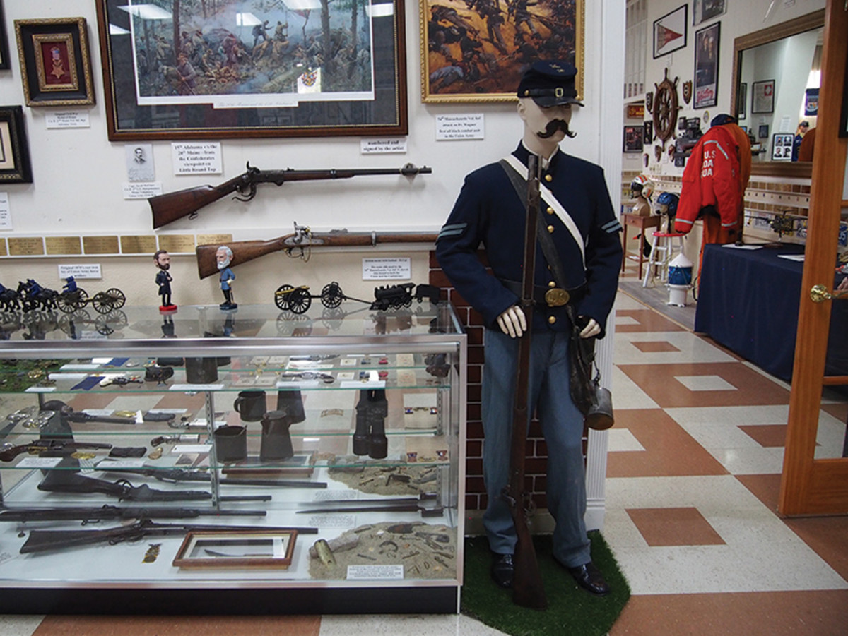 Civil War soldier stands next to a display of weapons, equipment and models from the era.