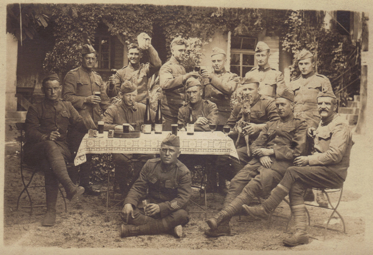 Most likely taken in the spring or early summer of 1919, the soldiers gathered here are enjoying some of the local wines and beers at an outdoor table. Although there is nothing written on the back of the photo, several of the soldiers have visible 1st Division patches thereby giving identity to  the group.