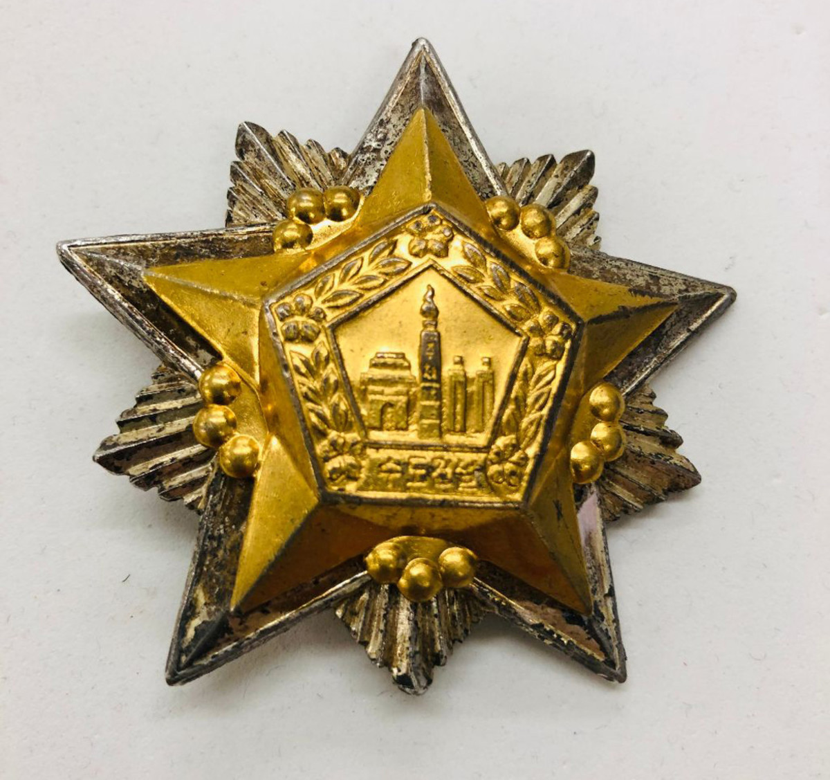 The Order of the Capital City Construction Commemoration is a 60mm wide badge with a gilt star superimposed over a large silver star with rays.