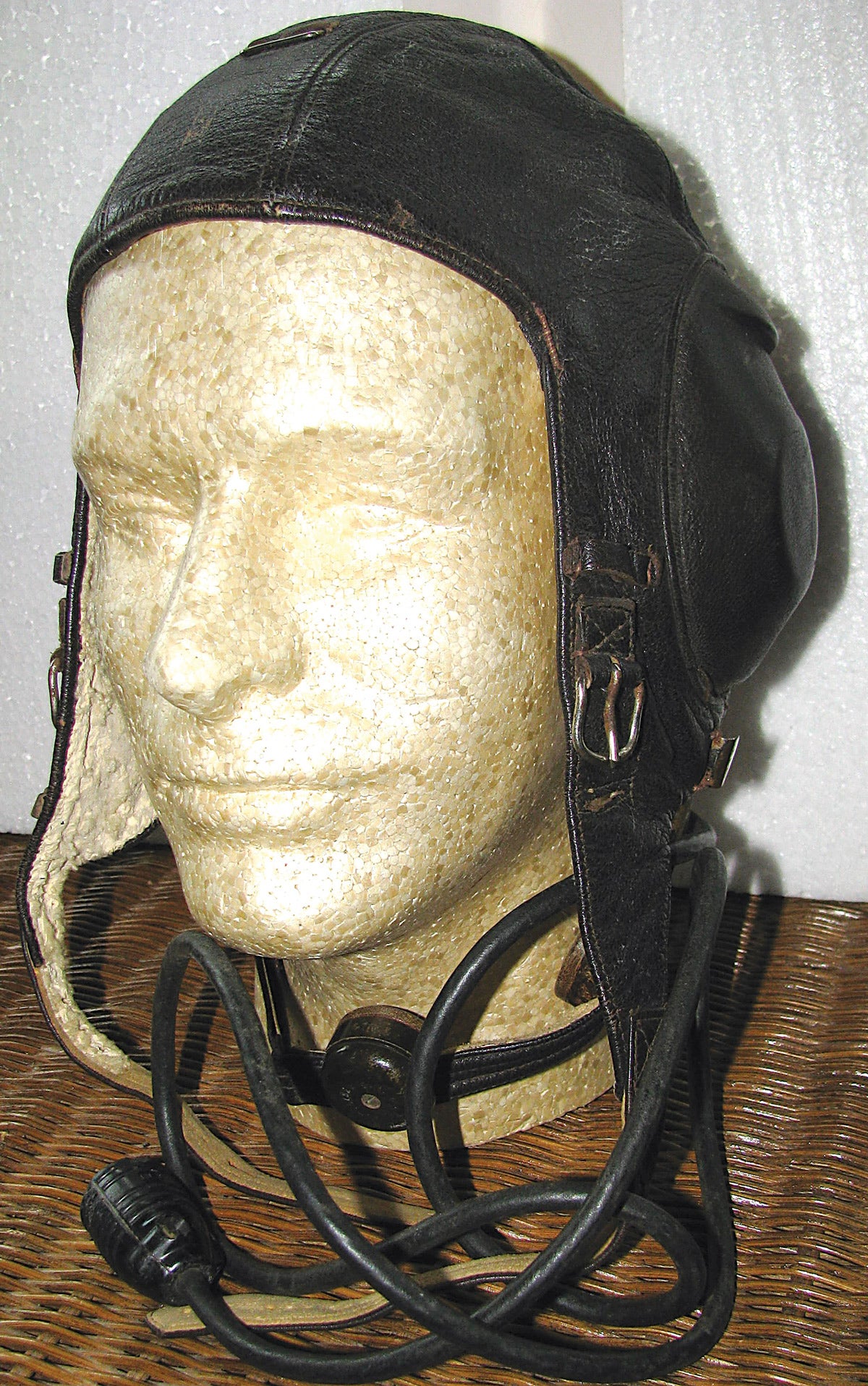 A full winter flying leather helmet complete with earphones sewn into the sides, and throat microphone. The inside is lined in cream-colored fleece with a manufacturer label sewn to the rear.
