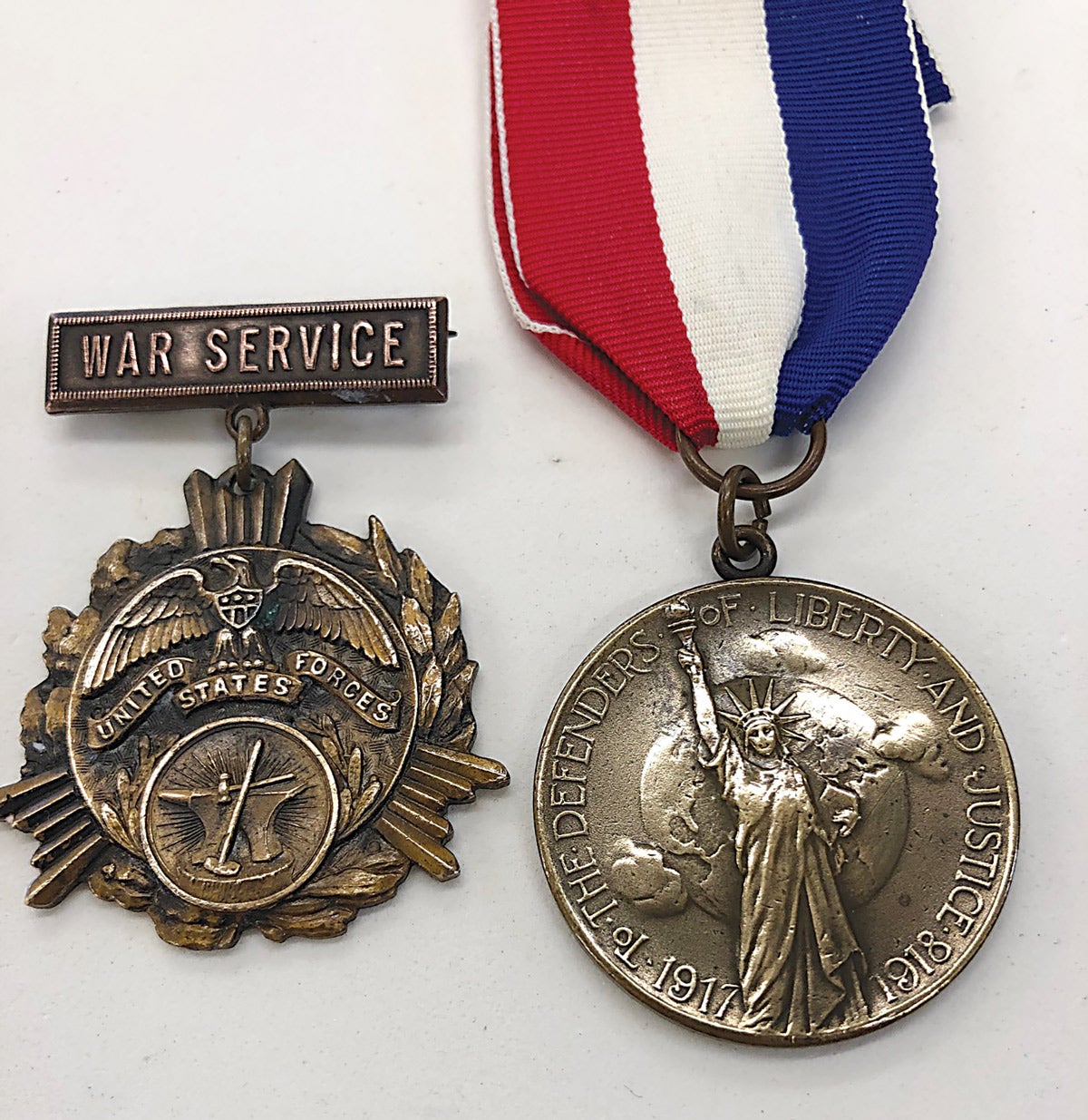 The circular image of an anvil and hammer identify the Blacksmith Medal and the silver General Fire Extinguisher Company medal shows the WWI dates 1917-1918 at the base of the Statue of Liberty.