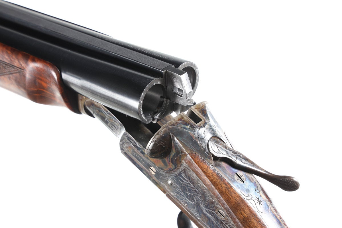 Closeup view of LC Smith Ideal Grade SxS 12 gauge shotgun, Serial #46725, manufactured in 1949. Checkered pistol grip stock with case-colored receivers with broad-leaf-engraved scenes with single Hunter trigger and ejectors. Full beavertail forearm with high solid rib with dual sight beads. All numbers are matching. Barrels are of London steel and have 3in chambers. Choked Full & Modified. Gun remains as new with some handling. Comes with numbers-matching shipping carton with numbers-matching hang tag.