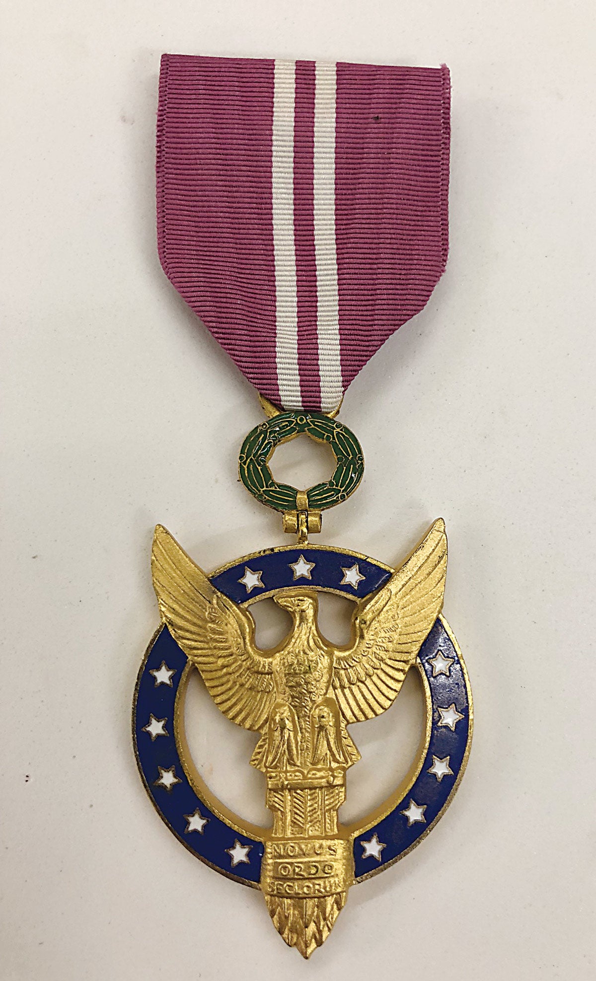 The gold base of the eagle on the Presidential Medal of Merit is inscribed “Novus Ordo Seclorum” meaning “a new Order of the ages” and is found on the reverse of the Great Seal of the United States.