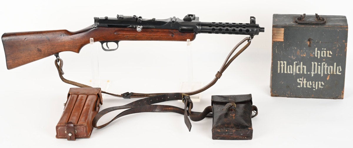 Fully transferable BATF-NFA Nazi-proof WWII Steyr-Solothurn MP-34 submachine gun package. Very fine 9mm gun is from a 1934-1940 production run and based on a design for the MP-19 by the Rheinmetall company of Dusseldorf, Germany. The MP-34 was manufactured from the very best materials available and finished to the highest possible standard, so much so that it earned the nickname ‘the Rolls-Royce of submachine guns.’ Package includes: submachine gun, parts kit, 9mm barrels, top cover, trigger guard, bolts with charging handles, WWII wooden ammo box for magazines, 3-cell magazine pouch with magazines, leather case cling kit with tools, and bag with trigger group parts. SMG retains 95% original finish with bright bore and strong rifling. Stock is serialized to the receiver and Nazi proofed. Estimate