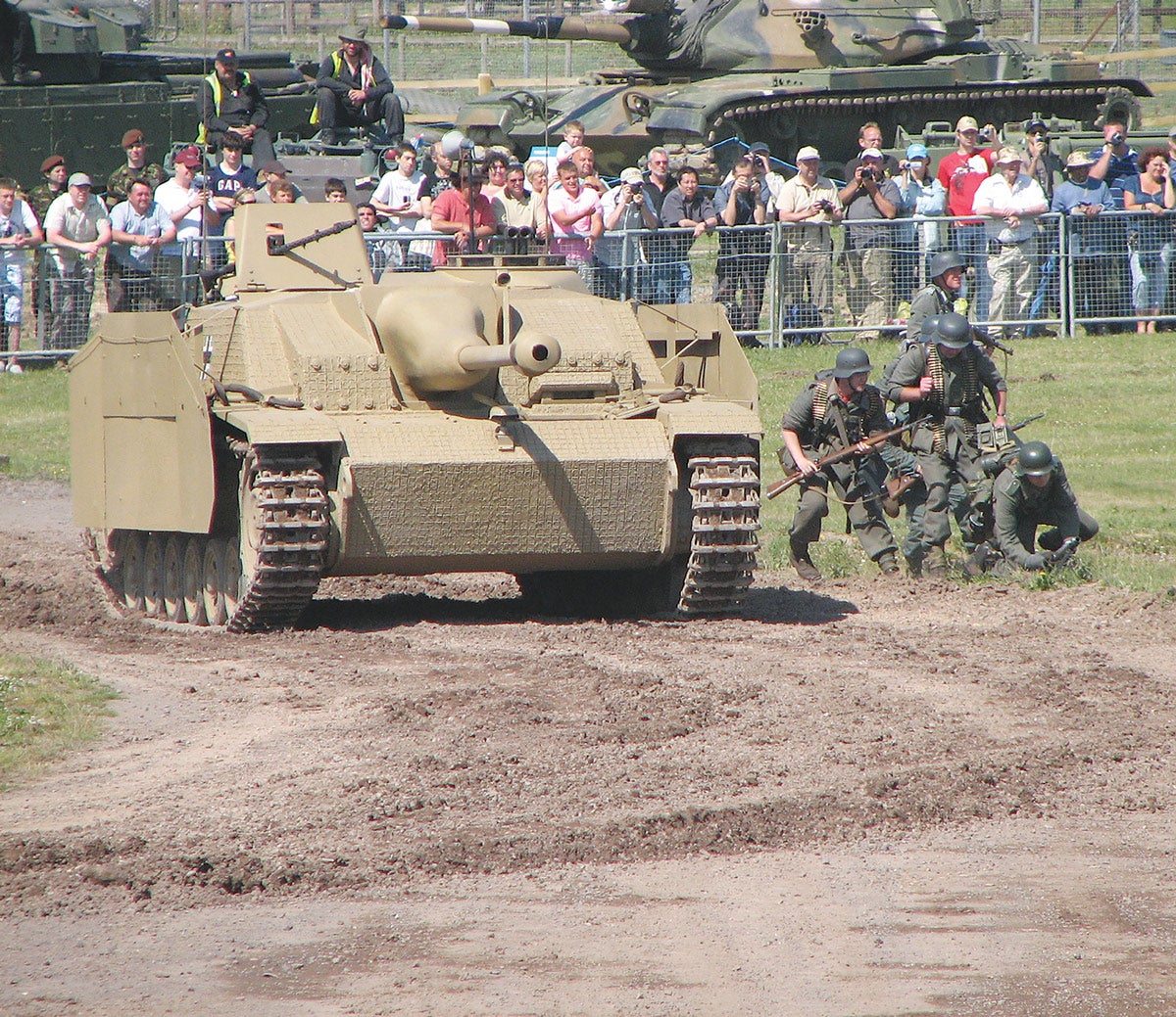 An arena display by an Ausf G in action with re-enactors depicting German infantry and giving some scale to its size.