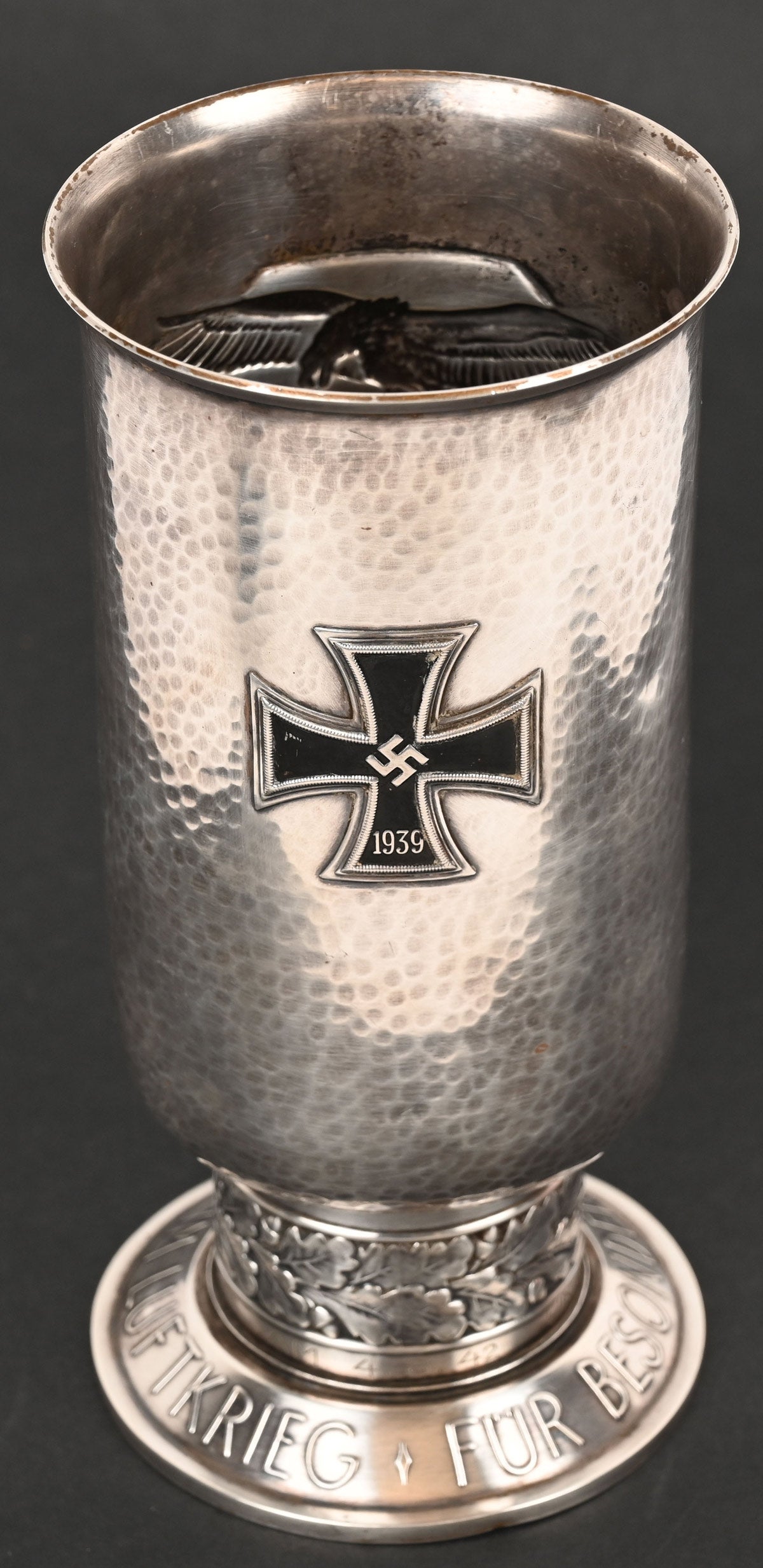 World War II Nazi German Luftwaffe honor goblet, second pattern (circa 1941/1942-1944), die-struck, three-piece, silver-plated, nickel-silver piece consisting of cup, stem and base. Cup has all-over ‘hammered’ surface with two embossed eagles engaged in aerial combat to the obverse and a 1939 Iron Cross to the reverse. Engraved with recipient’s name, rank and date of award ‘UNTEROFFIZIER HEINRICH THOLEN AM 4. 8. 42.’ Base embossed in script ‘Für Besondere Leistung im Luft krieg’ (For exceptional achievement in the air war).